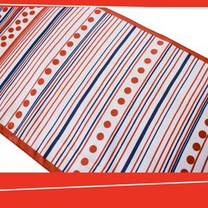 Pode incluir: Um caminho de mesa branco com um padr&atilde;o de listras vermelhas e azul marinho e bolinhas vermelhas. O caminho de mesa tem uma borda vermelha e est&aacute; em &acirc;ngulo diagonalmente na moldura.