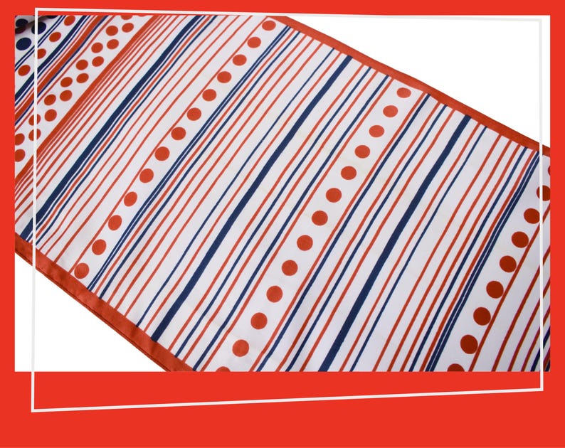 Pode incluir: Um caminho de mesa branco com um padr&atilde;o de listras vermelhas e azul marinho e bolinhas vermelhas. O caminho de mesa tem uma borda vermelha e est&aacute; em &acirc;ngulo diagonalmente na moldura.