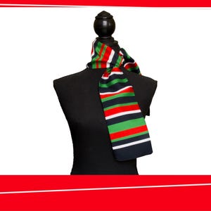May include: A striped scarf in green, red, white, and navy blue is draped over a black mannequin. The scarf's pattern features horizontal stripes of varying widths. The scarf is made of a soft, likely woven material.