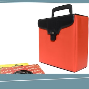 May include: A bright orange vinyl record carrying case with a black handle and top flap. The case is rectangular with a metal clasp. Two vintage record sleeves are in front of the case.