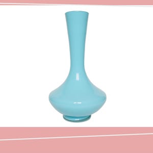Puede incluir: Un jarrón de cristal azul claro con base acampanada y cuello esbelto. El jarrón tiene un acabado liso y brillante y una forma redondeada y bulbosa. El jarrón es un objeto decorativo.