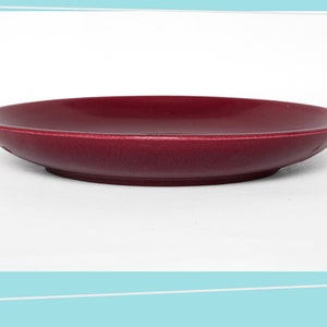 Puede incluir: Un platillo de cerámica de color rojo oscuro con un borde ligeramente redondeado.
