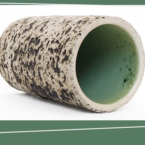 Puede incluir: Un jarrón cilíndrico de cerámica con un esmalte blanco y negro moteado. El interior del jarrón está esmaltado en un color verde claro.