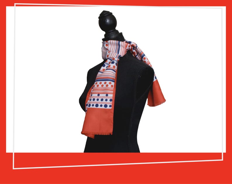 Pode incluir: Um len&ccedil;o estampado com um design vermelho, branco e azul est&aacute; drapeado sobre um manequim preto. O len&ccedil;o apresenta listras, pontos e uma borda com franjas. &Eacute; um acess&oacute;rio de moda.