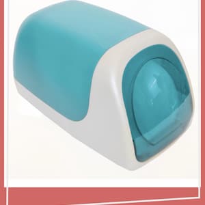 May include: A teal and white plastic dispenser with a rounded, elongated shape. The main body is teal with a white base and a translucent teal circular front panel that is slightly recessed into the white frame, creating a smooth, modern profile.