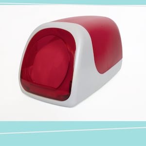 May include: A red and white plastic object with a rounded top and a transparent red front. The object has a white base and a curved design. The overall shape is rectangular with rounded edges.