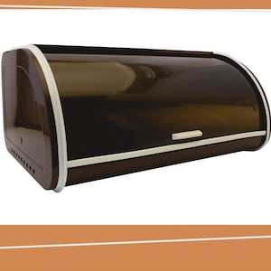 Op de afbeelding: Een donkerbruine broodtrommel met een roldeksel en een witte rand. De container heeft een rechthoekige basis met afgeronde hoeken, een kleine witte handgreep aan de voorzijde en een reeks kleine ventilatiegaatjes langs het zijpaneel.