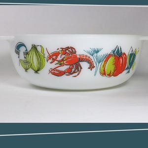 May include: White, vintage Pyrex bowl with a colorful seafood and vegetable design. The bowl features illustrations of a red lobster, green onions, and a red and yellow pumpkin. It has two small handles.