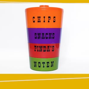 May include: A multi-colored plastic container with four sections for storing snacks. The sections are labeled "CHIPS", "SNACKS", "PINDAS", and "NOTEN".
