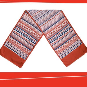 Pode incluir: Um len&ccedil;o vintage com um padr&atilde;o geom&eacute;trico arrojado. O len&ccedil;o apresenta listras e bolinhas em vermelho, branco e azul marinho sobre um fundo branco. As extremidades do len&ccedil;o s&atilde;o de cor laranja queimado s&oacute;lido com uma borda com franjas.