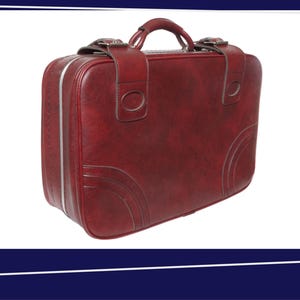 Peut inclure: Une valise vintage bordeaux avec une poignée et une garniture argentée. La valise est de forme rectangulaire avec des coins arrondis et des coutures décoratives. Elle comporte une poignée supérieure et deux fermetures à boucle.