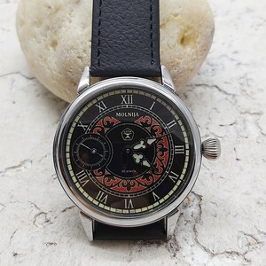 May include: A silver wristwatch with a black face and red and black patterned design. The watch face has Roman numerals and the words "MOLNIJA" and "16 jewels".