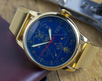 Puede incluir: Un reloj dorado con una esfera azul y una correa de malla. La esfera presenta símbolos masónicos y el texto "КОЛЛЕКЦИЯ" y "АНТИКВАРНАЯ".