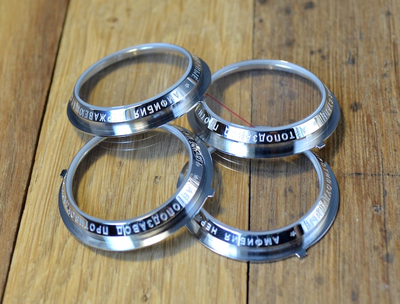 May include: Four silver watch bezels with clear glass inserts. The bezels are engraved with the words "AMPHORA", "TOMONOVA", "ПРОИЗВОДСТВО", and "ХКАБЕДОН".