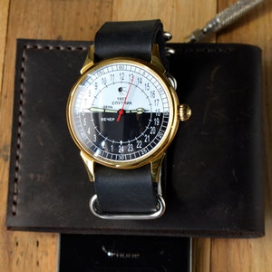 May include: A gold-tone wristwatch with a black leather band. The watch face is white with black markings and features the text "1957 Спутник" and "День Вечер".