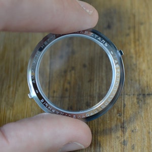 May include: A silver watch case back with the text "AMFIBIA + СТАЛЬ АВТОПОДЗАВОД + НЕРЖАВЕЮЩАЯ" engraved around the edge.