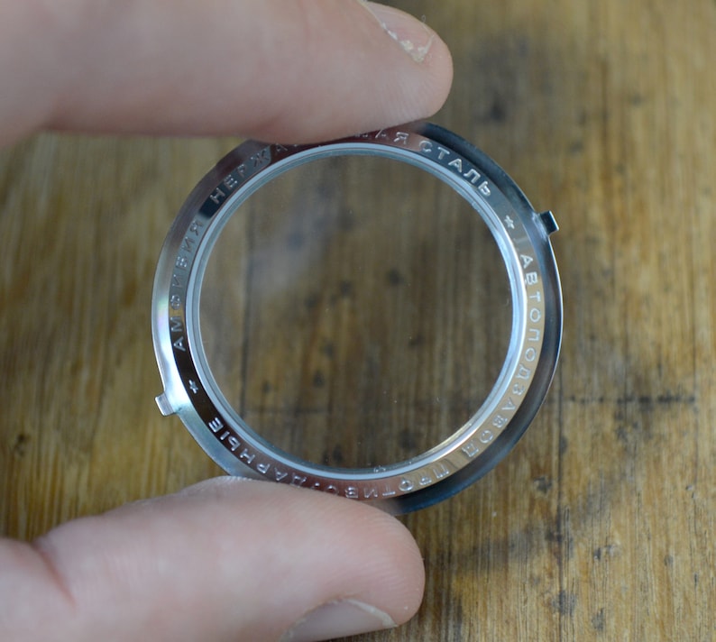 May include: A silver watch case back with the text "AMFIBIA + СТАЛЬ АВТОПОДЗАВОД + НЕРЖАВЕЮЩАЯ" engraved around the edge.