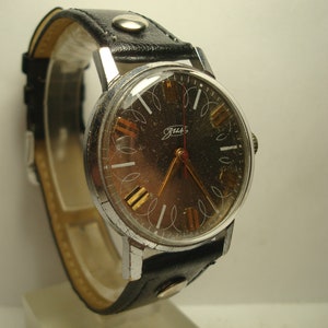 May include: A silver wristwatch with a black leather strap. The watch face has a black background with white Roman numeral hour markers and a gold second hand. The watch face also has the word "Zarya" printed on it.