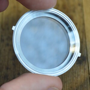 May include: A silver-colored metal filter with a round, flat base and a raised rim. The filter is designed to fit into a coffee maker.