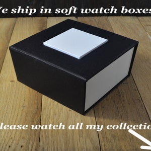 May include: A black watch box with a white lid. The box is made of soft material and is perfect for storing and protecting a watch. "We ship in soft watch boxes" and "Please watch all my collection" are written on the image.
