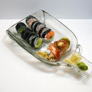 May include: Sushi rolls with avocado and shrimp are arranged on a clear, bottle-shaped glass plate. Ginger and wasabi are in a small dish. The sushi is a Japanese cuisine.