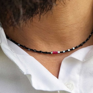Peut inclure: Un collier de perles noires et argentées avec une seule perle rouge au centre.