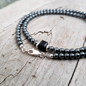 May include: A black hematite beaded necklace with a black onyx square pendant and a silver clasp.