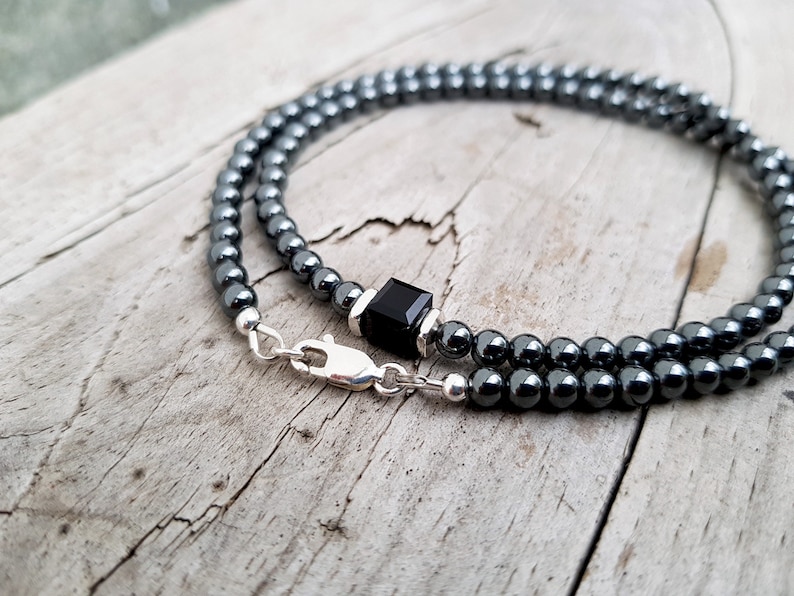 May include: A black hematite beaded necklace with a black onyx square pendant and a silver clasp.