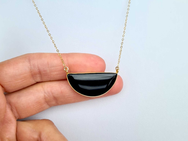 Pu&ograve; includere: Una collana con catena dorata e un ciondolo a forma di mezza luna nera.