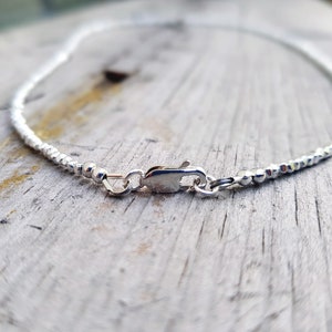 collana elegante e sottile, perfetta per uomo o donna, composta da pepite in argento solido ed al centro un piccolo cristallo in tre colori a scelta tra nero, verde smeraldo e blu zaffiro.