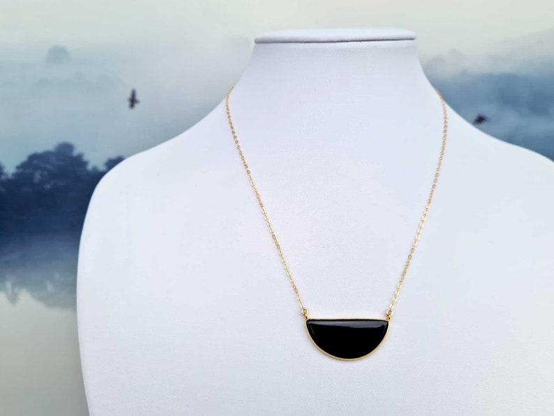 Pu&ograve; includere: Una collana con catena dorata e un ciondolo a forma di mezza luna nera.