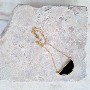 Pu&ograve; includere: Una collana con catena dorata e ciondolo a forma di mezzaluna nera.