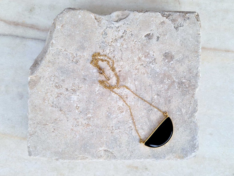 Pu&ograve; includere: Una collana con catena dorata e ciondolo a forma di mezzaluna nera.