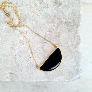 Pu&ograve; includere: Una collana con catena dorata e un ciondolo nero a forma di semicerchio.