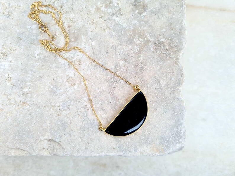 Pu&ograve; includere: Una collana con catena dorata e un ciondolo nero a forma di semicerchio.