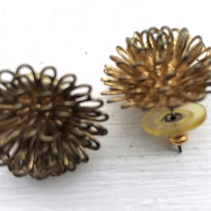 May include: Two vintage gold-toned metal earrings. Each earring features a spherical design made of looped wire, resembling a spiky ball. One earring has a post and a yellow earring back.