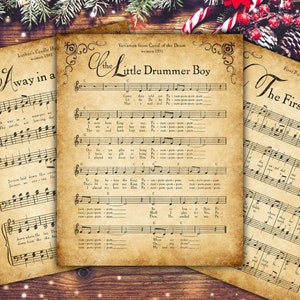 May include: Three vintage-style sheet music prints with Christmas carols. The titles include "I Way in a", "The Little Drummer Boy", and "The First Noel". The prints have a sepia tone and are arranged on a wooden surface with festive decorations.