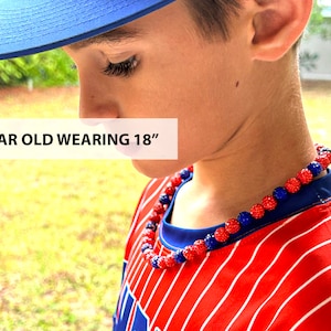 May include: An 8 year old wearing an 18 inch red and blue beaded necklace. The necklace is made of small, round beads with a sparkly finish.