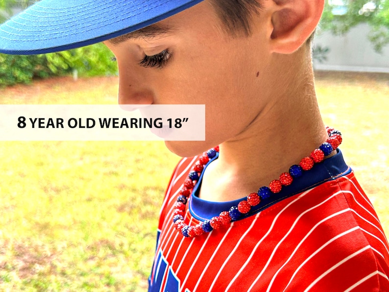 May include: An 8 year old wearing an 18 inch red and blue beaded necklace. The necklace is made of small, round beads with a sparkly finish.