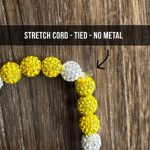 May include: A yellow and white beaded bracelet with a stretch cord and a tied knot closure. The bracelet is made with small, round beads that are covered in rhinestones. The text "STRETCH CORD - TIED - NO METAL" is visible at the top of the image.