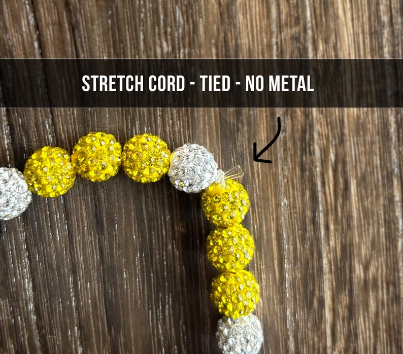 May include: A yellow and white beaded bracelet with a stretch cord and a tied knot closure. The bracelet is made with small, round beads that are covered in rhinestones. The text "STRETCH CORD - TIED - NO METAL" is visible at the top of the image.