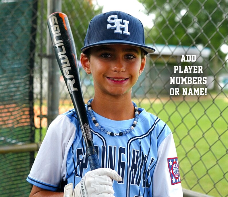 May include: A young baseball player wearing a blue and white baseball uniform with a blue hat that says "SH" on it. He is holding a black and silver baseball bat with the word "RADLIGS" on it. The player is standing in front of a chain link fence. The text "ADD PLAYER NUMBERS OR NAME!" is visible in the background.