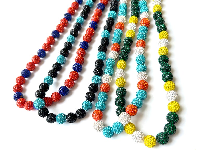 May include: Five strands of colourful beaded necklaces with sparkly accents. The necklaces are made of small, round beads in shades of black, red, blue, turquoise, green, white, and yellow.