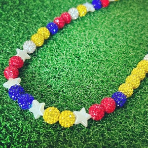 May include: A colorful beaded necklace with red, white, blue, and yellow beads. The beads are interspersed with white star-shaped beads.