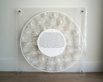 May include: A white acrylic framed ketubah with a floral design and Hebrew text. The ketubah is a Jewish marriage contract.