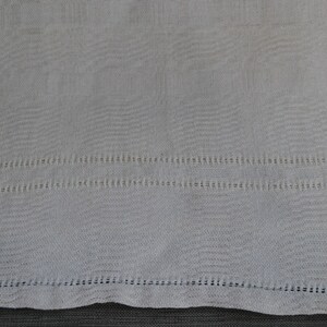 May include: A white cotton tea towel with a delicate embroidered border. The towel has a subtle texture and is perfect for drying dishes or hands.