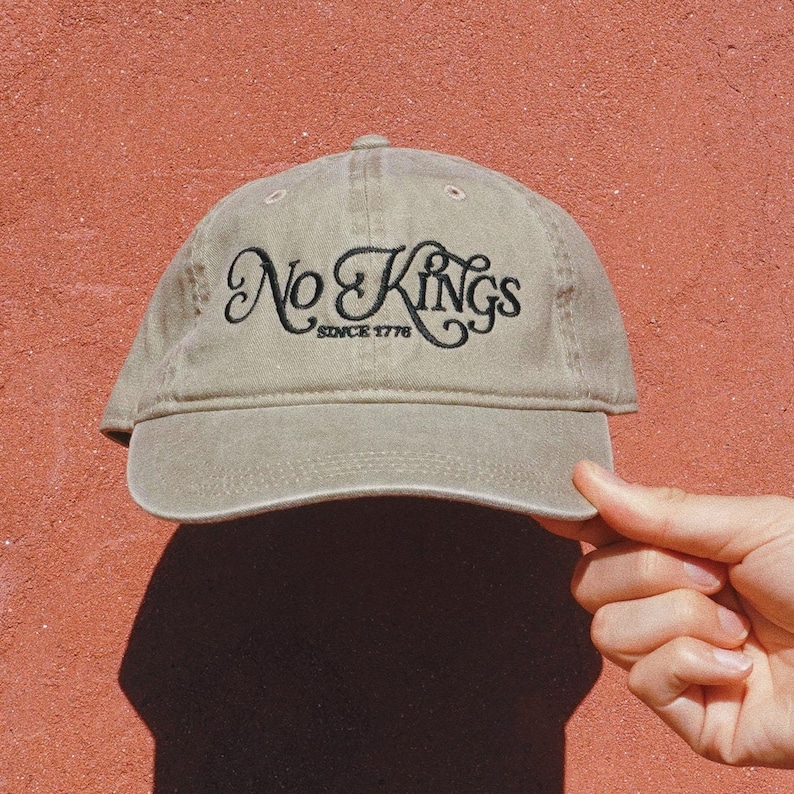 Pode incluir: Bon&eacute; de beisebol c&aacute;qui com o texto bordado "No Kings Since 1776" em escrita preta. O bon&eacute; &eacute; exibido em um fundo vermelho.