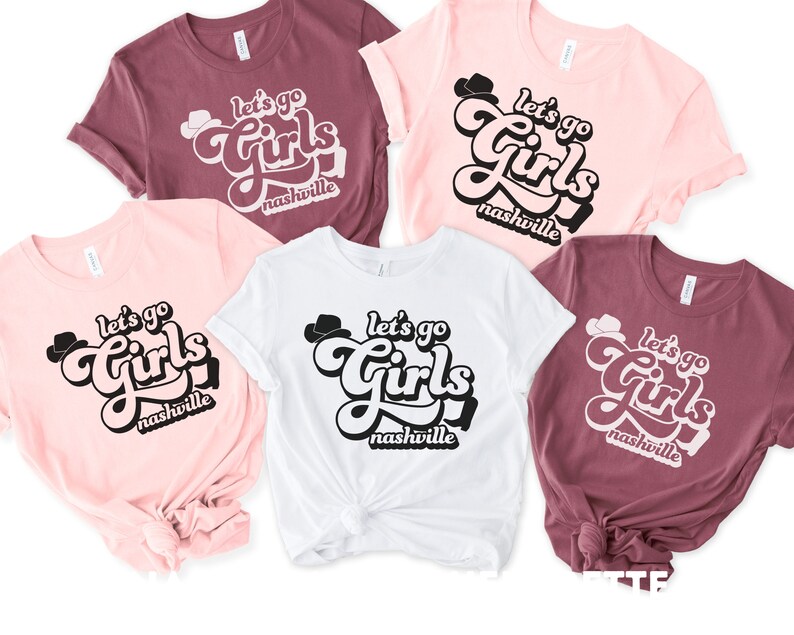 May include: Five t-shirts with the text "Let's go Girls Nashville" in a retro font. The shirts are in pink, white, and maroon.