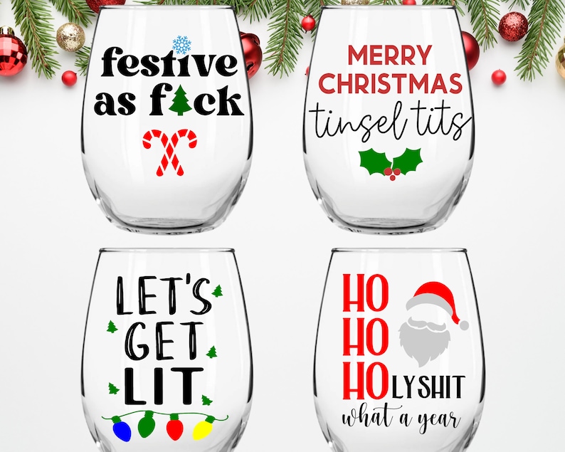 May include: Four stemless wine glasses with humorous Christmas-themed text printed on them. The glasses feature the phrases "festive as f*ck", "Merry Christmas tinsel tits", "Let's get lit", and "Ho Ho Ho LYSHIT what a year".
