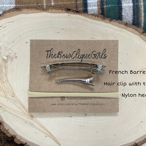 May include: A set of hair accessories, including a French barrette, a hair clip with teeth, and a nylon headband, displayed on a wooden surface. The brand name "The Bow Clique Girls" is printed on a brown card.